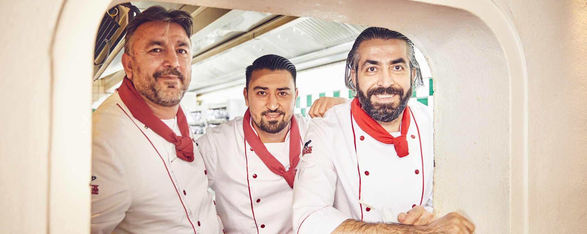 BLOCK HOUSE Köche Drei Block House Köche schauen aus einer Küchendurchreiche